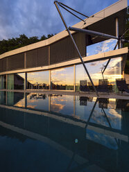 Switzerland, glass front of modern villa at dusk with terrace and pool in the foreground - LAF02076