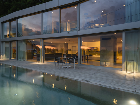 Schweiz, beleuchtete moderne Villa in der Abenddämmerung mit Terrasse und Pool im Vordergrund, lizenzfreies Stockfoto