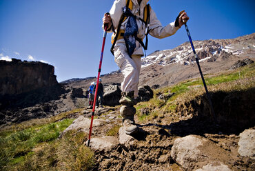 Ein Wanderer mit Trekkingstöcken überquert einen kleinen Bach auf dem Kilimandscharo. - AURF01961