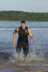 Ein männlicher Athlet, der beim Training für einen Triathlon aus dem Wasser steigt. - AURF01962