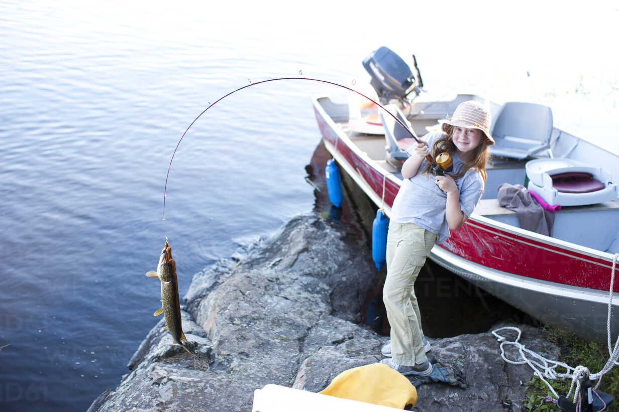A little girl holds a fishing pole with a large fish on the end of the fishing  line with the boat in the background. stock photo