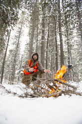 Ein männlicher Jäger wärmt sich an einem Feuer im Schnee. - AURF01986