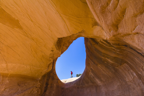 Ein Mann wandert, eingerahmt von einem natürlichen Felsbogen., lizenzfreies Stockfoto