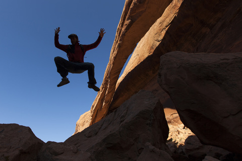 Ein Mann springt neben einem natürlichen Felsbogen in die Luft., lizenzfreies Stockfoto