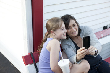 Eine Mutter und ihre Tochter sitzen auf einer Bank und nehmen ein Selbstporträt mit einem Handheld-Gerät auf. - AURF02031