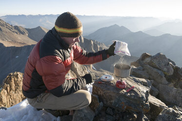 Ein Mann kocht Wasser auf einem Campingkocher auf dem Gipfel des Mount Wilson bei Tellride, Colorado. - AURF02034