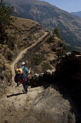 Ein Trekker steigt in Nepal eine steile Steintreppe am Hang hinunter. - AURF02064