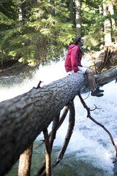 A young man sits on a log over a waterfall in Idaho. - AURF02103