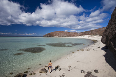 Ein junges Mädchen im Bikini spaziert an einem einsamen Strand neben dem klaren, blauen Wasser der Sea of Cortes außerhalb von La Paz, Baja California Sur, Mexiko. - AURF02110