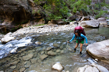 A woman uses a trekking pole to cross a section of the Virgin River during a backpacking trip through the Narrows in Zion National Park, in Springdale, Utah. - AURF02112
