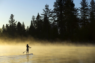 Die Silhouette einer Frau, die bei Sonnenaufgang im Nebel auf dem Lake Tahoe, Kalifornien, Stand Up Paddleboarding (SUP) betreibt. - AURF02113