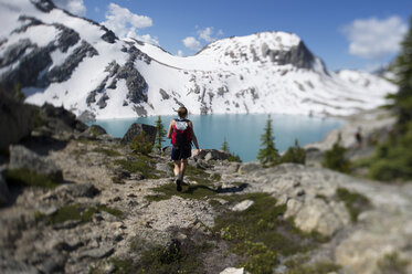 A young woman hiker walks towards a lake. - AURF02132