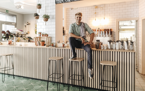 Junger Mann arbeitet in seinem Start-up-Café und sieht zuversichtlich aus, lizenzfreies Stockfoto