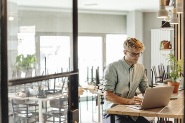 Junger Mann bei der Arbeit in seinem Start-up-Café, mit Laptop - GUSF01244