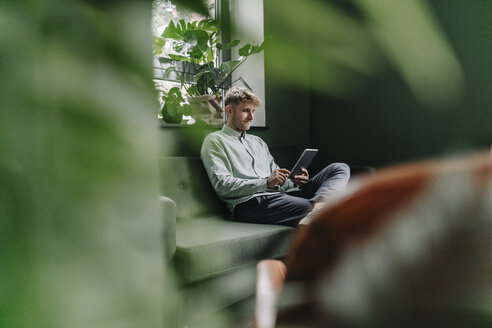 Young man sitting on green couch, using digital tablet - GUSF01251