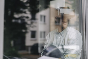 Junger Mann sitzt am Fenster und benutzt eine VR-Brille - GUSF01257