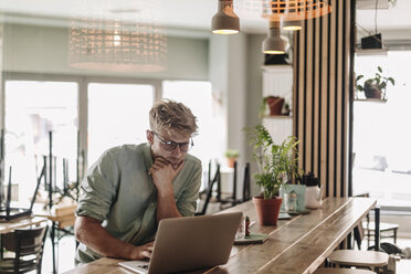 Junger Mann bei der Arbeit in seinem Start-up-Café, mit Laptop - GUSF01261