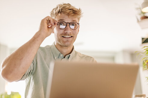 Junger Mann, der einen Laptop benutzt und durch seine Brille schaut - GUSF01264