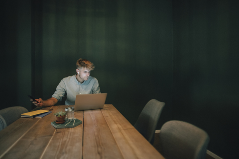 Mann sitzt im Büro, arbeitet bis spät in sein Start-up-Unternehmen und hört Musik, lizenzfreies Stockfoto