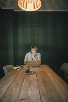 Mann sitzt im Büro, arbeitet bis spät in sein Start-up-Unternehmen, benutzt Laptop und Smartphone - GUSF01270