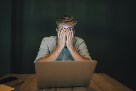 Müder Mann, der in seinem Büro sitzt, spät in seinem Start-up-Unternehmen arbeitet und sich die Augen zuhält, lizenzfreies Stockfoto