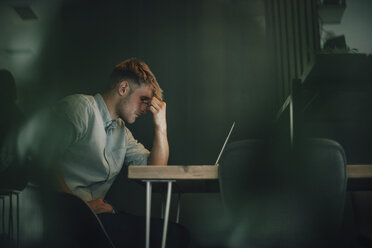 Tired man sitting in office, working late in his start-up company - GUSF01273