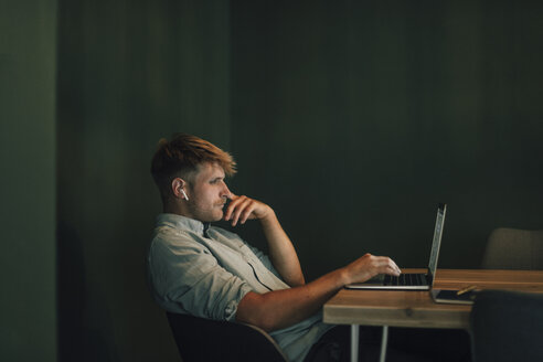 Man sitting in office, working late in his start-up company, listening music - GUSF01275