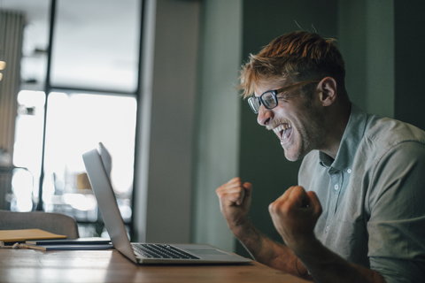 Junger Mann mit Laptop, lacht fröhlich, lizenzfreies Stockfoto