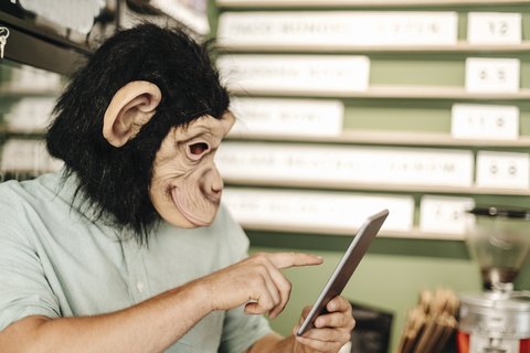 Mann mit Affenmaske, der ein digitales Tablet benutzt, lizenzfreies Stockfoto