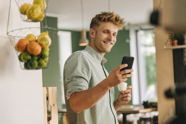 Young business owner drinking coffee, checking smartphone - GUSF01297