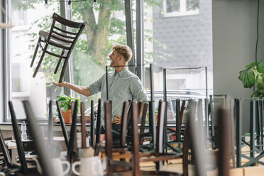 Mann balanciert Stuhl auf der Hand, schließt sein Café - GUSF01298