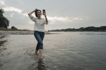 Lachende Frau, die am Flussufer läuft und Selfies macht - KNSF04351