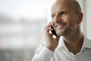Ein lächelnder Geschäftsmann steht in seinem Büro und telefoniert mit seinem Handy - KNSF04361