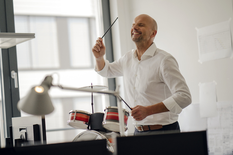 Businessman making noise with drums in his office stock photo