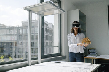 Woman holding architectural model of house, using VR glasses - KNSF04385