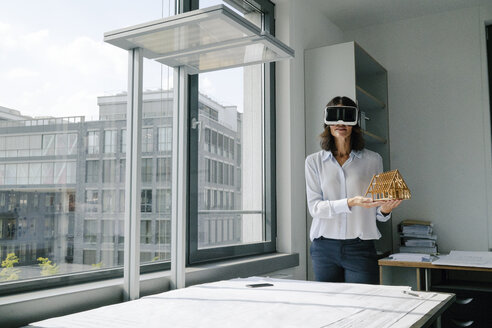 Frau hält Architekturmodell eines Hauses und benutzt eine VR-Brille - KNSF04385