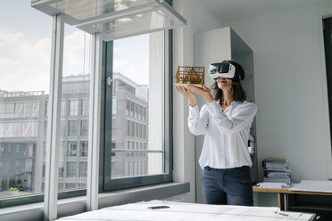 Woman holding architectural model of house, using VR glasses - KNSF04386