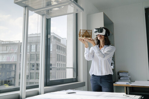 Frau hält Architekturmodell eines Hauses und benutzt eine VR-Brille - KNSF04386