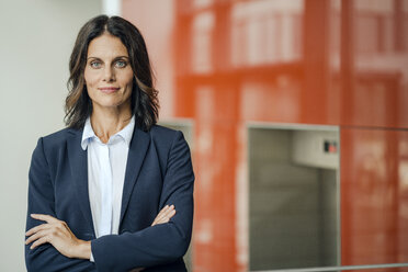 Portrait of a successful businesswoman, standing in front of elevator, with arms crossed - KNSF04389