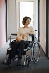 Disabled business woman sitting in wheelchair, with laptop on knees - KNSF04395