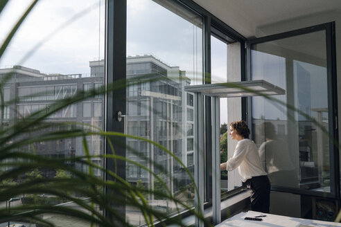 Businesswoman standing in office, looking out of window - KNSF04397