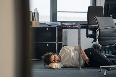 Tired businesswoman sleeping on floor under her desk - KNSF04401