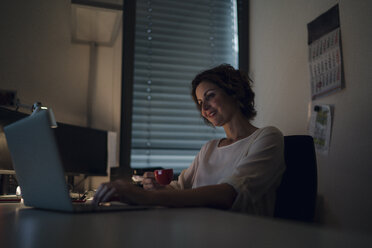 Geschäftsfrau, die Überstunden macht, einen Laptop benutzt und Kaffee trinkt - KNSF04403