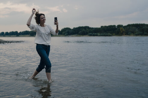 Lachende Frau, die am Flussufer läuft und ihr Smartphone benutzt - KNSF04408