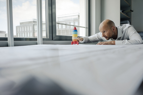 Businessman playing with toy rocket in office stock photo