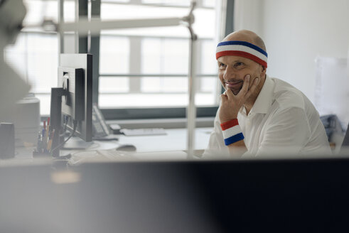 Businessman sitting in office, wearing sweat bands - KNSF04433