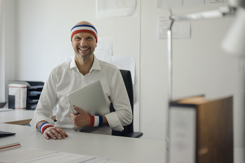 Geschäftsmann sitzt im Büro, trägt Schweißbänder, hält Laptop, lizenzfreies Stockfoto