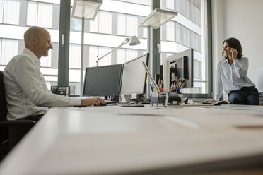 Businessman and woman working together in office - KNSF04443