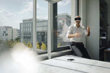 Geschäftsmann, der in seinem Büro steht und eine VR-Brille benutzt - KNSF04458