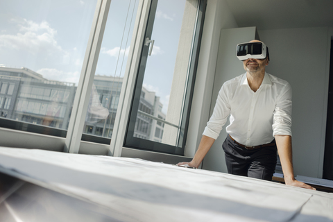 Geschäftsmann, der in seinem Büro steht und eine VR-Brille benutzt, lizenzfreies Stockfoto